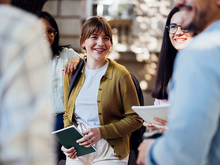 Smiling student holding a notebook talking to fellow students on campus