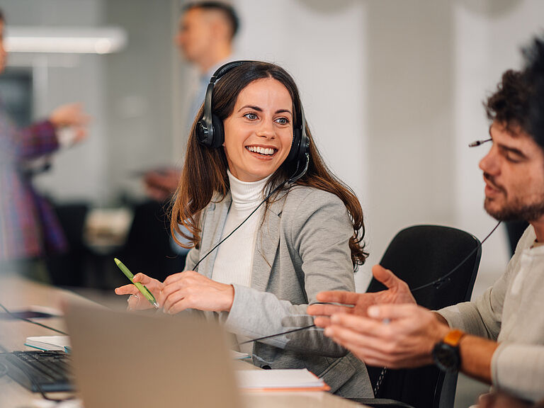 Smiling advisor with headset talking with a colleague at her desk