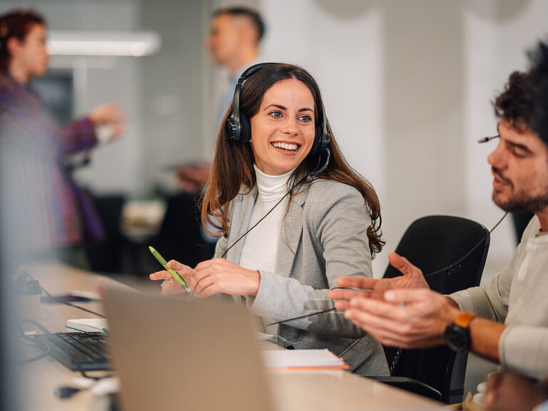 Smiling advisor with headset talking with a colleague at her desk