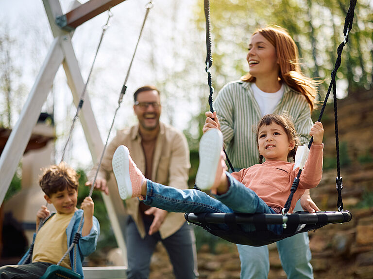 Famille heureuse avec deux enfants s’amusant ensemble sur une balançoire dans un parc
