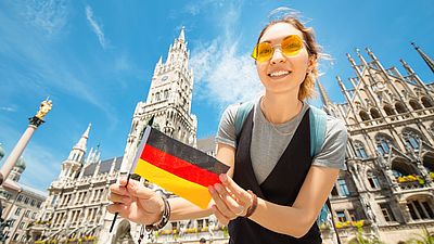 Internationale Studentin lächelt mit einer deutschen Flagge in der Hand in München