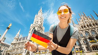 Chica estudiante internacional sonriendo con una bandera alemana en la mano en Múnich