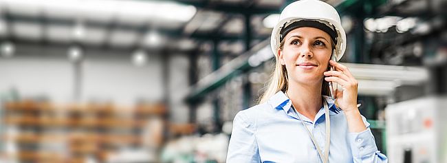 Junge Frau mit einem weißen Helm auf dem Kopf telefoniert mit ihrem Handy