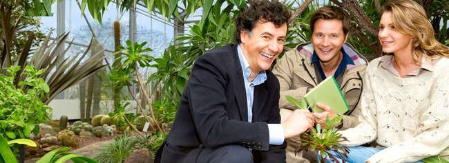 Two men and a woman look at a plant in the botanical garden