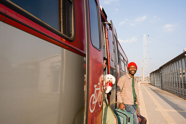 Smiling young man with a suitcase stepping off a train at a sunny station
