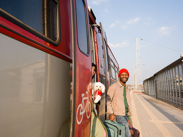 Joven sonriente con maleta bajando de un tren en un andén soleado