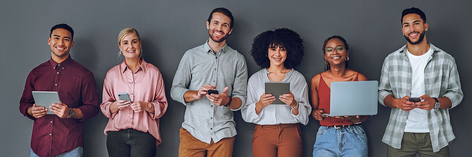 Grupo internacional de jóvenes con dispositivos electrónicos buscando vacantes laborales