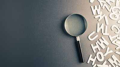 A magnifying glass and paper letters on a desk