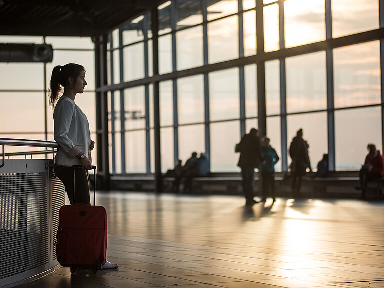 Entry to Germany. Female traveler with a rolling suitcase stands in a modern airport area at sunset.