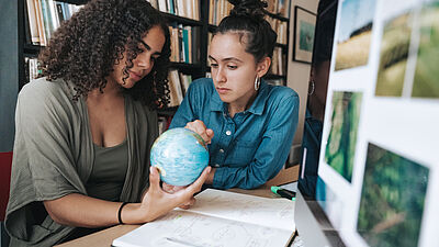 Zwei junge Frauen schauen auf einen Globus