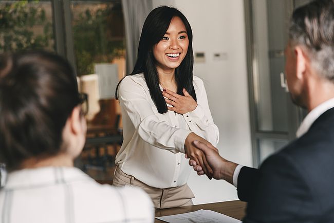 Two business partners in office shaking hand of a young woman