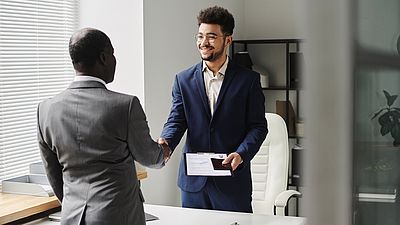 Especialista del centro de visados felicitando a un hombre por la obtención del visado, de pie y dándose la mano.