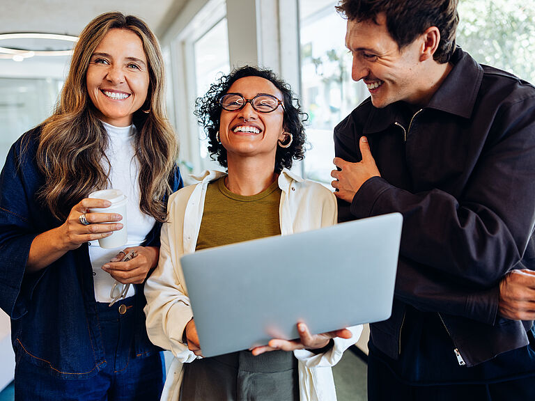 Tres compañeros de trabajo sonrientes mirando juntos un portátil en la oficina
