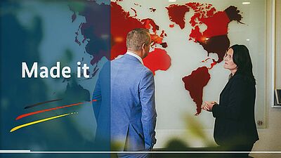 Zwei Personen von hinten /seitlich vor Weltkarte, links Schriftzug "Made it"