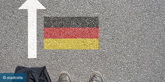 Asphalt mit einem weißen Pfeil nach oben, einer Deutschlandflagge und zwei Füßen in Schuhen